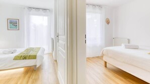 A hotel room with two beds, a wooden floor, a white wall, and a picture on the wall.