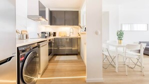 A modern kitchen with stainless steel appliances, a built-in oven, and a dishwasher. There is a dining area with a white table and chairs.