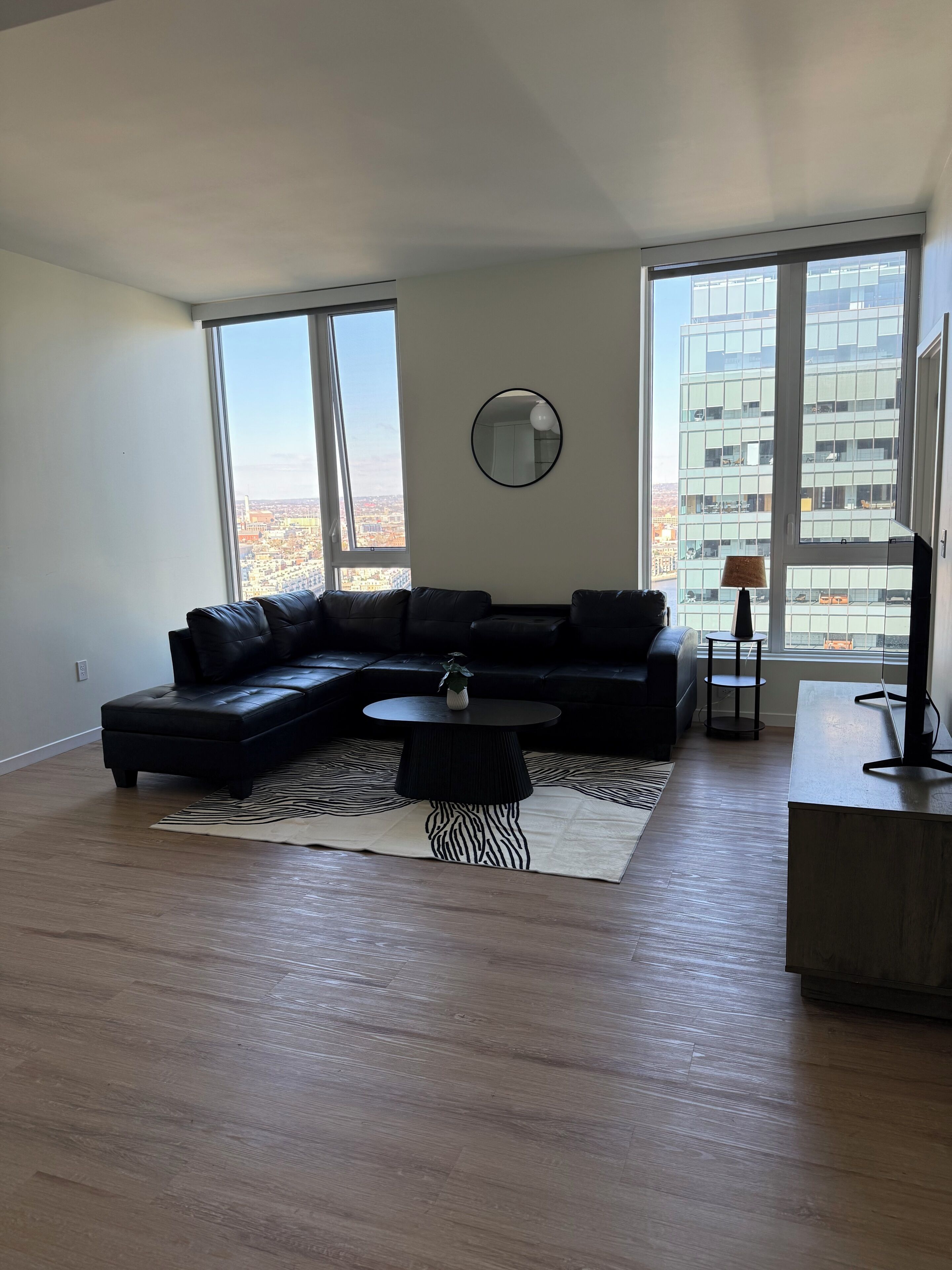 A modern living room with a sectional sofa, a round coffee table, a zebra-patterned rug, a round mirror, and a TV stand.
