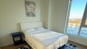 Un dormitorio con una cama, una mesita de noche, un ventanal con vistas y un cuadro en la pared.
