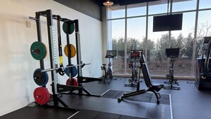 Un gimnasio con equipo de levantamiento de pesas, bicicletas estáticas y un amplio ventanal.