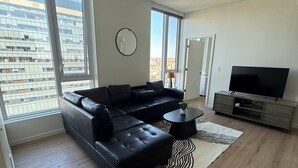 Una sala de estar moderna con un sofá modular, un televisor de pantalla plana y grandes ventanales con vistas a la ciudad.