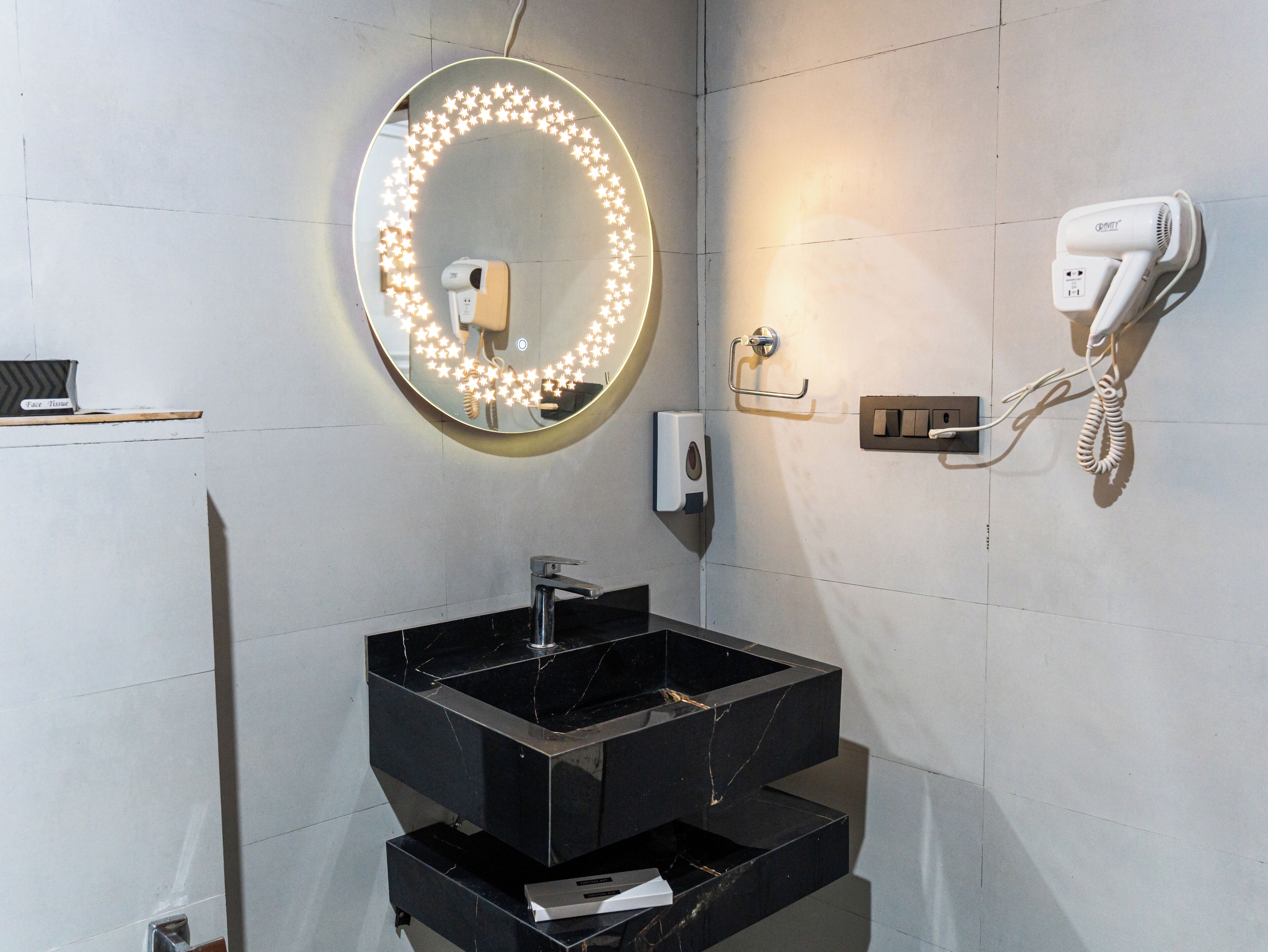 A bathroom with a round mirror, a hairdryer, and a soap dispenser.