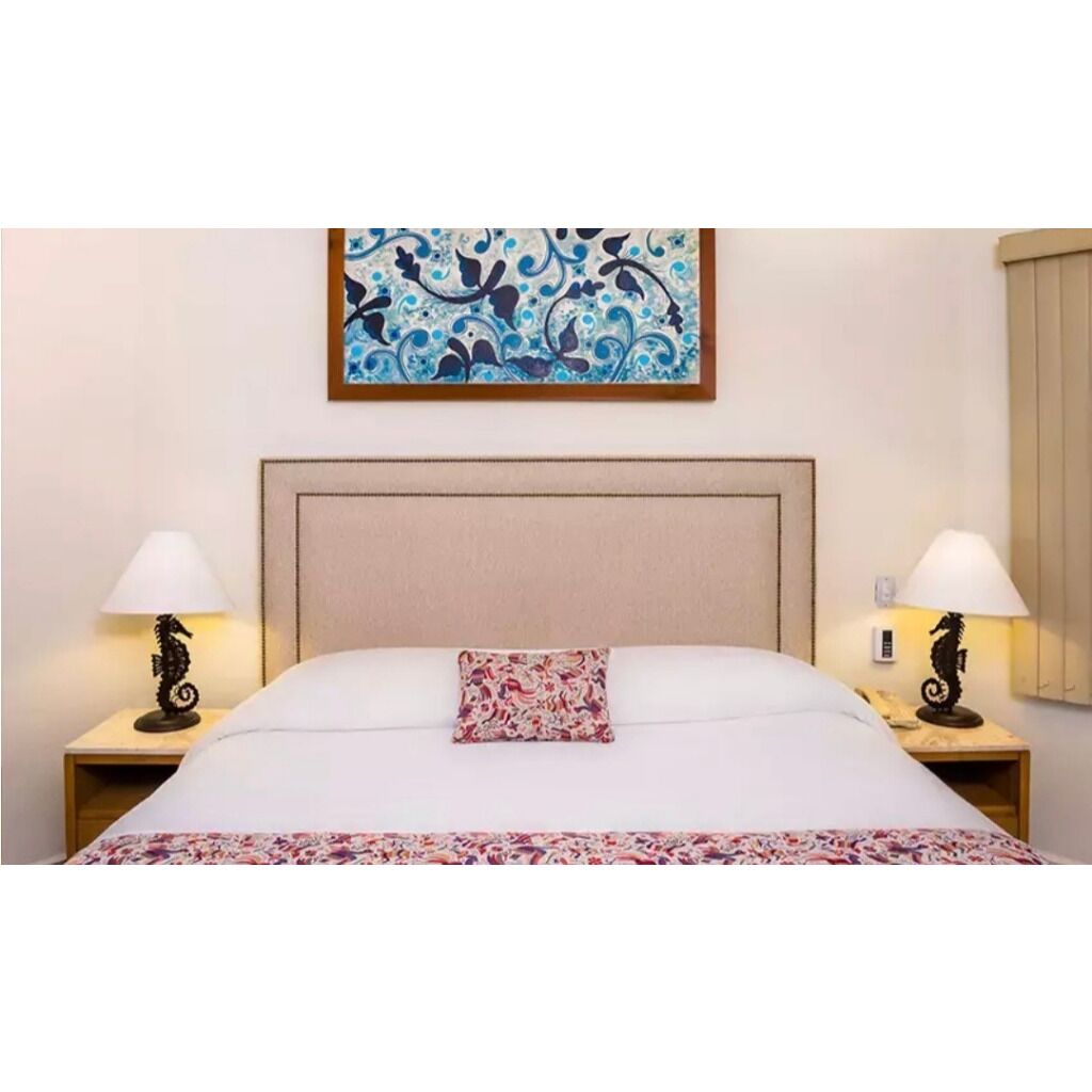 Habitación de hotel con una cama, dos mesitas de noche con lámparas, un cabecero y una obra de arte enmarcada sobre la cama.