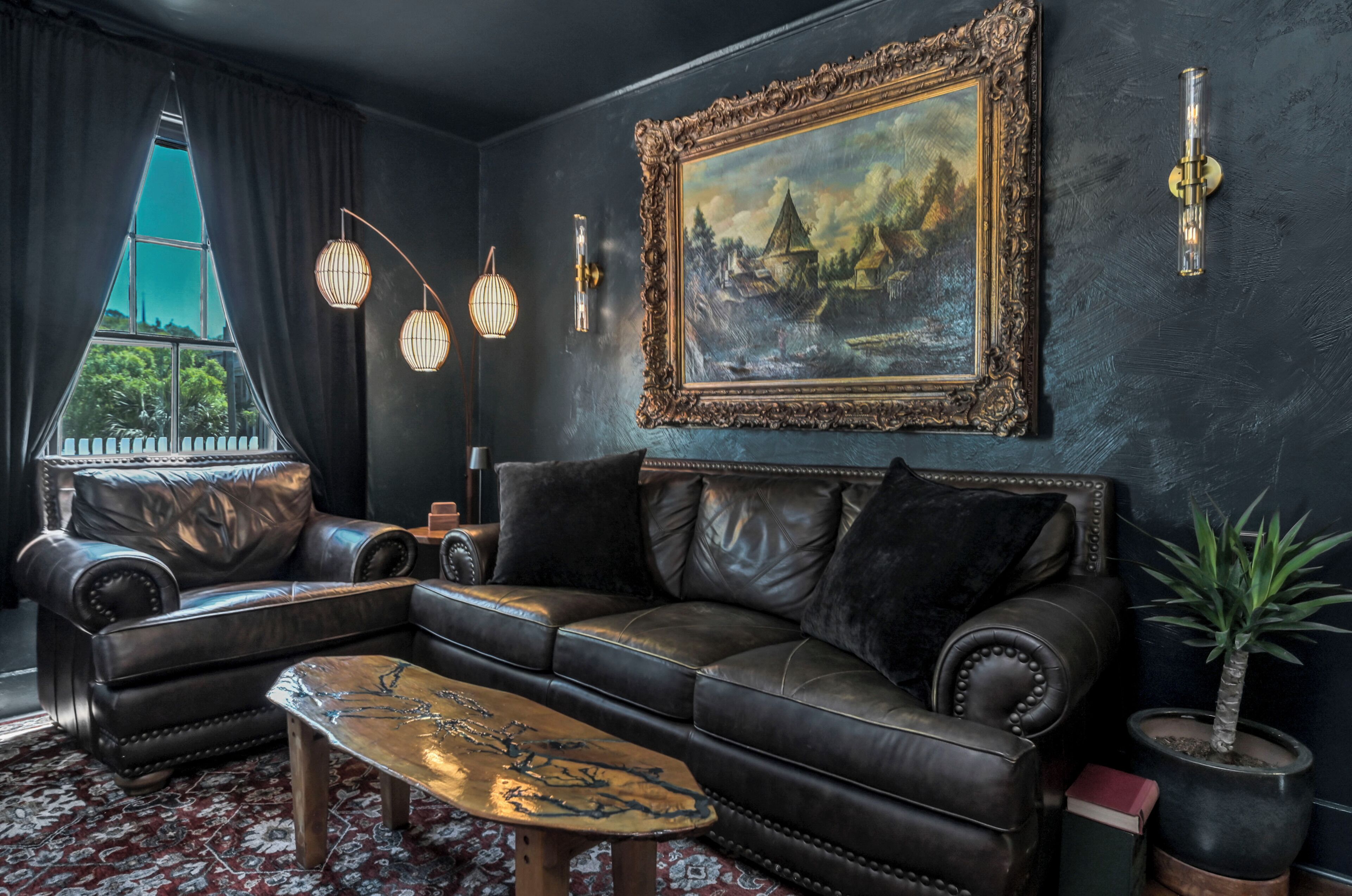 Ein wohnzimmer im dunklen Stil mit einem Ledersofa, einem Couchtisch, einem gerahmten Gemälde und einem Topf mit Pflanze.