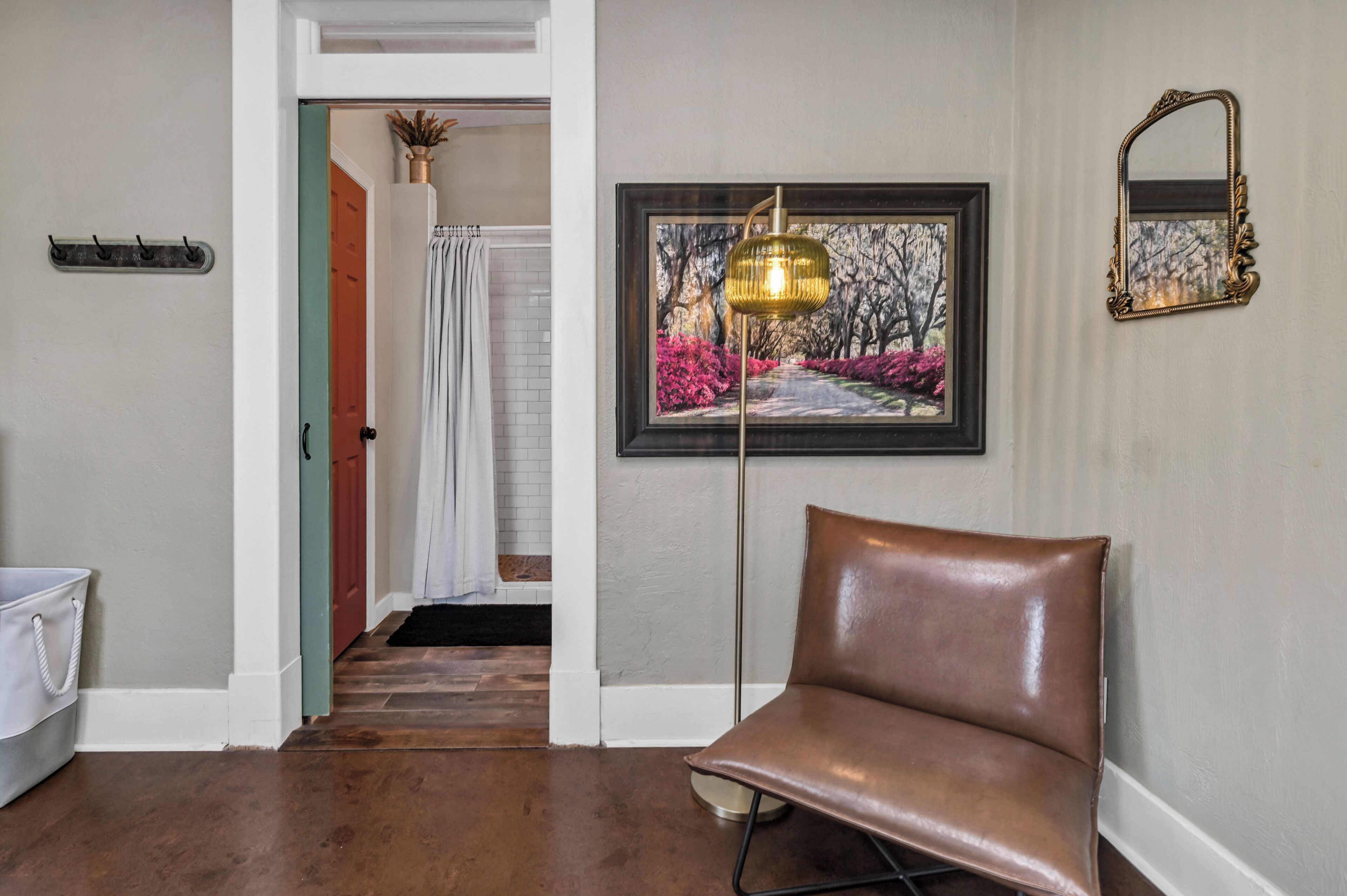 A hallway with a brown leather chair, a framed painting, a floor lamp, a mirror, and a door leading to another room.