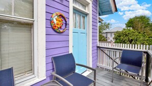Ein lilafarbenes Haus mit einer blauen Tür, einem weißen Zaun und zwei blauen Stühlen auf der Veranda.