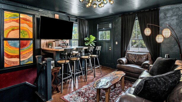 Ein modernes Wohnzimmer mit Ledersofa, Couchtisch, Fernseher und Essbereich mit Stühlen und einer Pflanze.