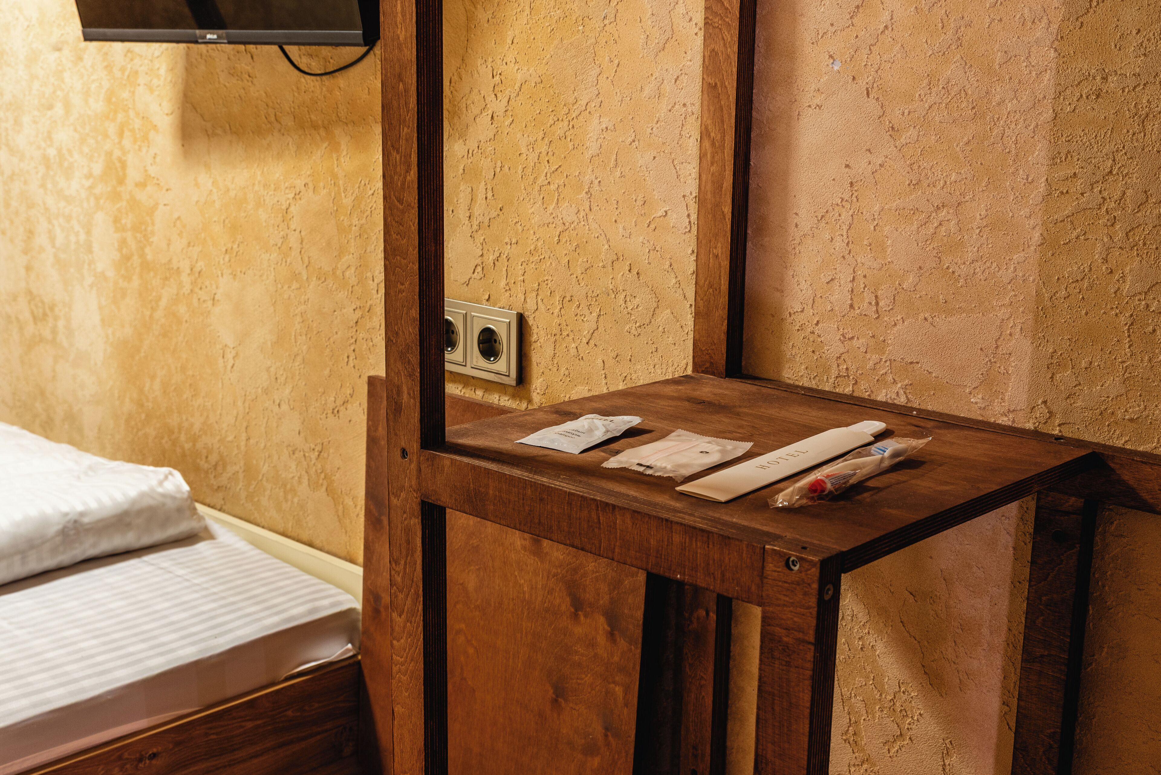 A wooden bedside table with a power outlet and a television mounted on the wall.