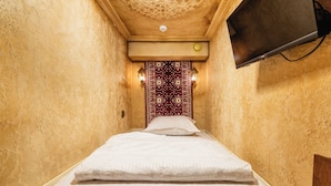 A narrow hotel room with a bed, a television mounted on the wall, and a decorative wall pattern.
