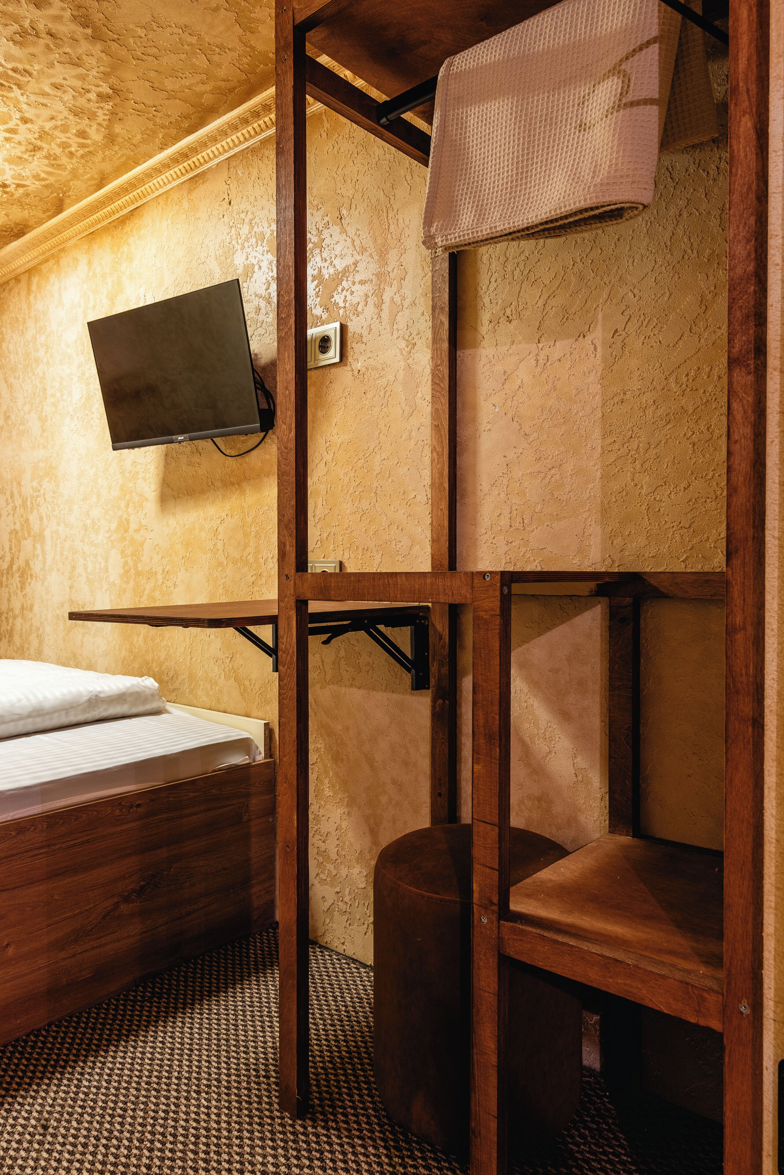 A bunk bed room with a television mounted on the wall, a wooden desk, and a small stool.