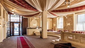 A hotel lobby with a red carpet, ornate columns, and a view of the street.