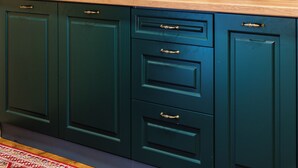 A kitchen with teal cabinets, a coffee maker, and a patterned backsplash.