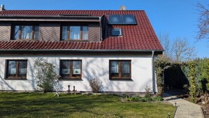 A two-story house with a red-tiled roof, multiple windows, and a small garden area.
