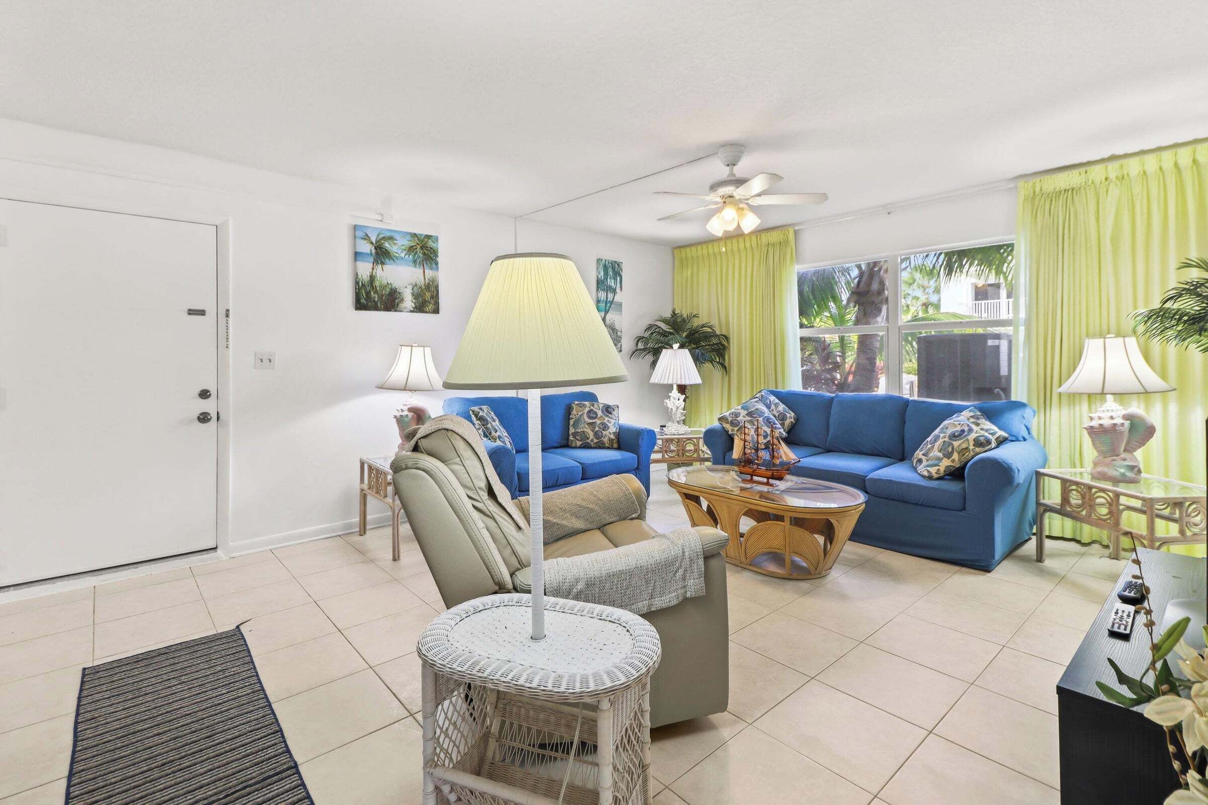 A living room with a blue sofa, a round wicker coffee table, a ceiling fan, and a green curtain.