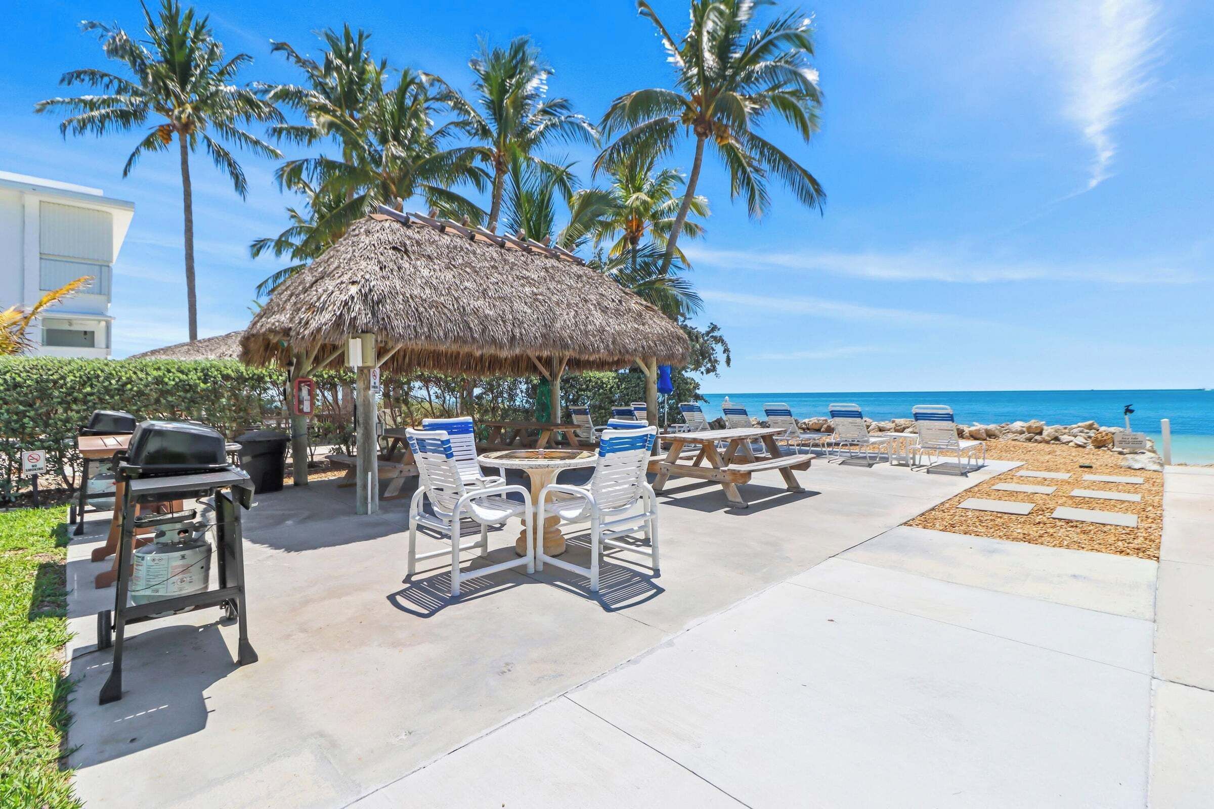 A beachside patio with a thatched-roof table, chairs, and a grill.