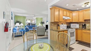 A modern kitchen with wooden cabinets, a microwave, stove, and a dining area with a glass table and chairs. - The perfect tropical sanctuary with turquoise waters and steps from the beach. (Key Colony Beach)