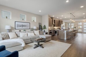 A modern living room with a sofa, a coffee table, and a kitchen area with a bar and island. - Modern 4BR Englewood | Hot Tub + EV Charger (Englewood)