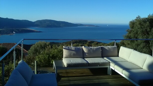 Ein Balkon mit einer weißen Couch und Blick auf das Meer und die Hügel.