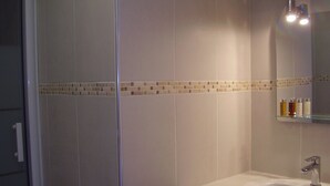 Ein Badezimmer mit Duschkabine aus Glas, einem weißen Waschbecken mit Spiegel darüber und einer gefliesten Rückwand.