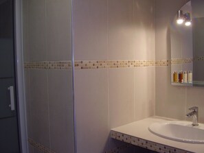 Ein Badezimmer mit Duschkabine aus Glas, einem weißen Waschbecken mit Spiegel darüber und einer gefliesten Rückwand.
