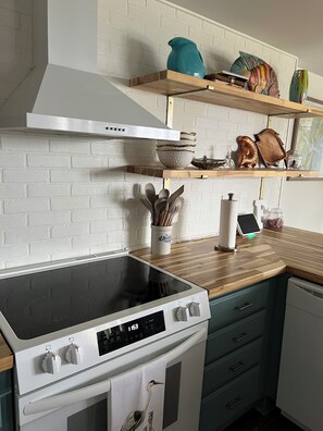 A kitchen with a white brick wall, wooden shelves, a white stove, and a teal vase.