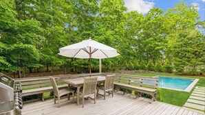 A wooden deck with a table and chairs, a grill, and a pool. - Classic 4-bedroom Home in East Hampton, Minutes from Town (East Hampton)