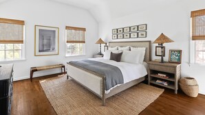 A bedroom with a bed, bedside tables, a bench, and a large window with blinds. - Classic 4-bedroom Home in East Hampton, Minutes from Town (East Hampton)