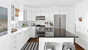 A modern kitchen with white cabinetry, stainless steel appliances, a marble countertop, and a black island with stools. - Classic 4-bedroom Home in East Hampton, Minutes from Town (East Hampton)