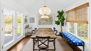 A dining area with a wooden table, chairs, a bench, a hanging light fixture, and a large window with a view of the outdoors. - Classic 4-bedroom Home in East Hampton, Minutes from Town (East Hampton)