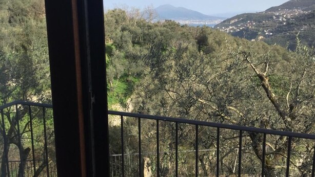 A balcony with a view of a hilly landscape, trees, and distant buildings.