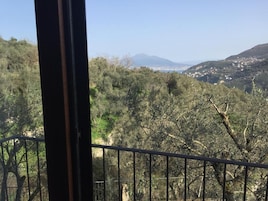 Un balcón con vistas a un paisaje montañoso, árboles y edificios al lejano.