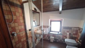 A bathroom with a shower, two toilets, a window, and a tiled floor.