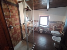 Un baño con ducha, dos inodoros, una ventana y suelo de baldosas.