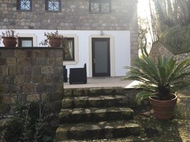 Un edificio de piedra con fachada blanca, una puerta negra y escalones que llevan a una silla negra.