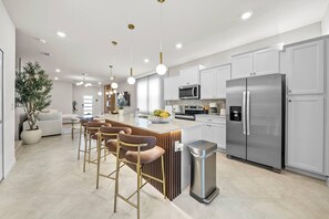 Una cocina moderna con una isla central, taburetes de bar, electrodomésticos de acero inoxidable e iluminación colgante.