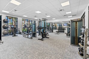 Ein modernes Fitnessstudio mit unterschiedlichen Trainingsgeräten, großen Fenstern und einem Teppichboden.