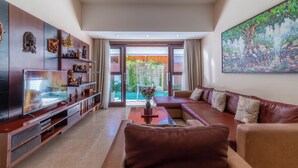 A modern living room with a large flat-screen TV, leather sofas, a coffee table, and decorative wall art. - Nauli Villas Sanur (Denpasar)