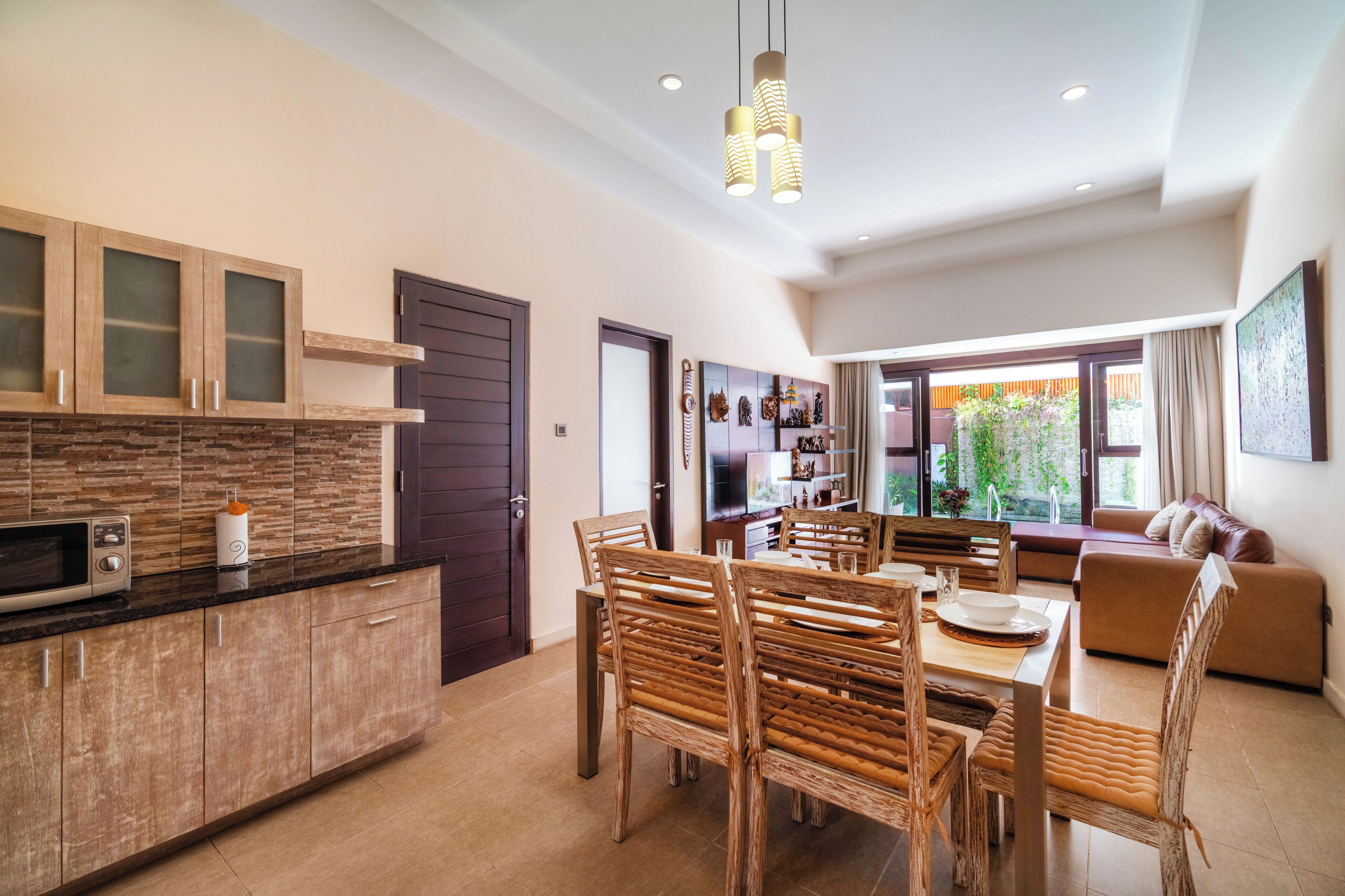 Una cocina moderna con armarios de madera, un comedor con mesa y sillas, y una sala de estar con sofá y un ventanal grande.