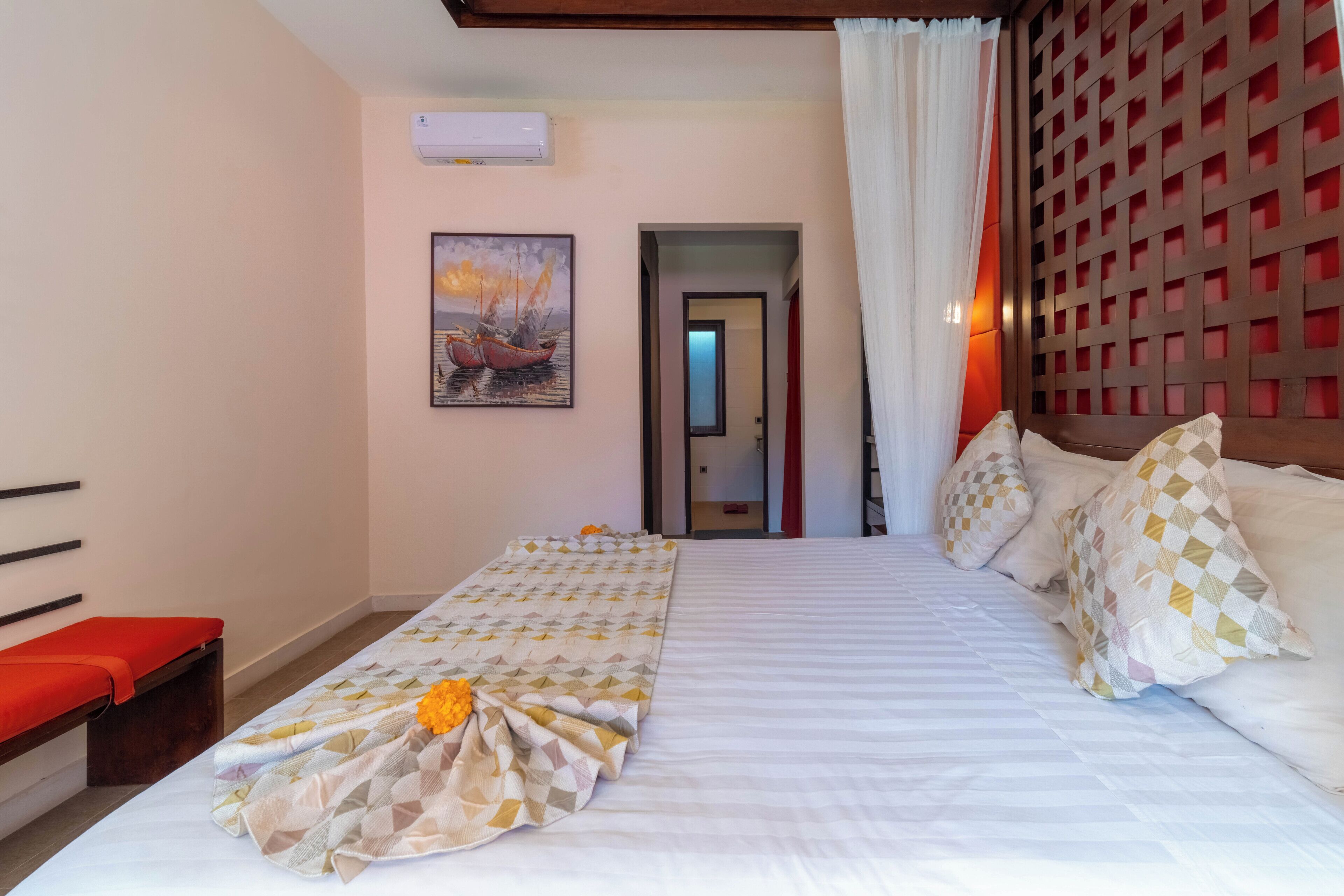 Une chambre d’hôtel avec un lit, un banc, un tableau et une porte donnant sur une autre pièce.