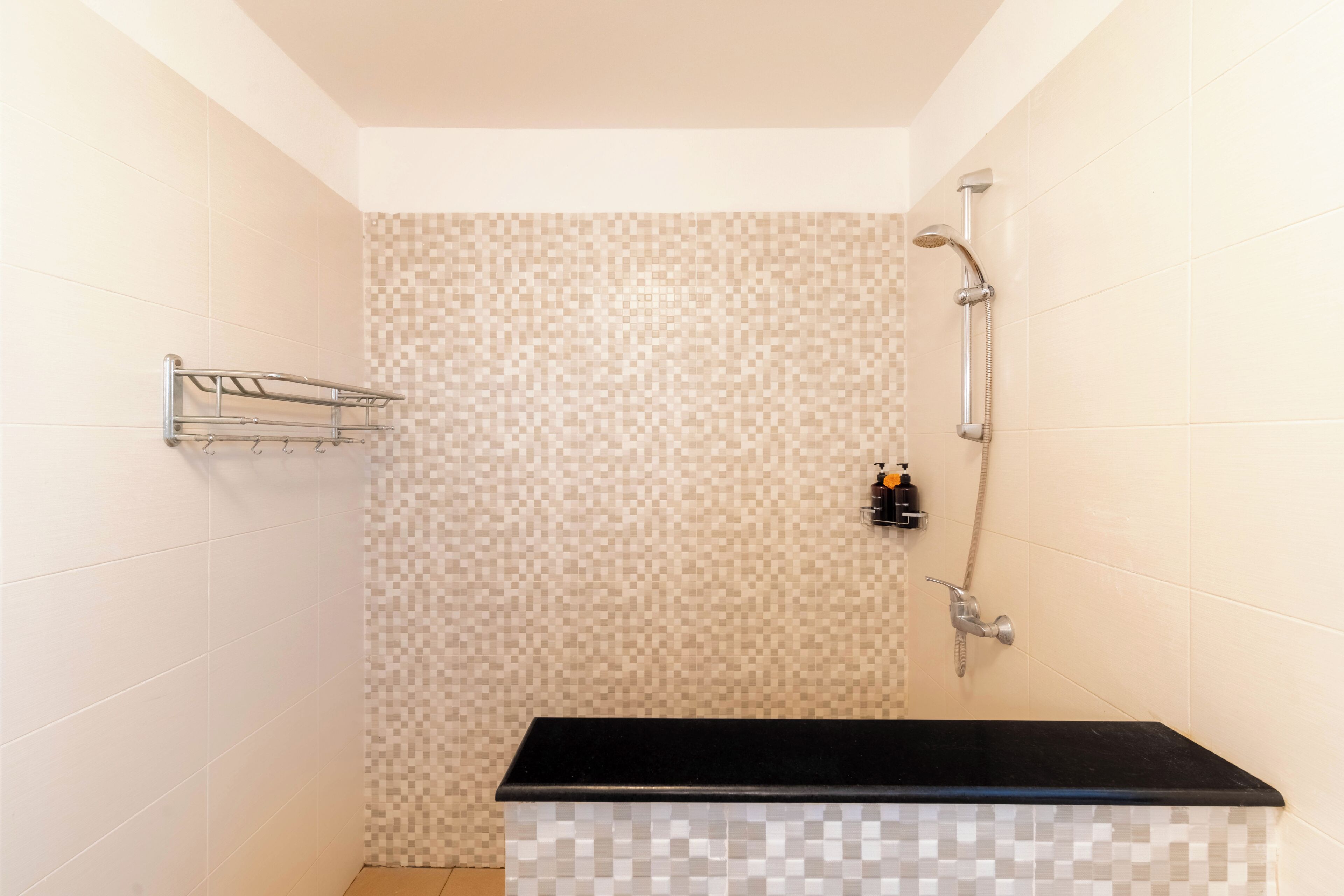 A shower with a tiled wall, a black countertop, and a metal rack.