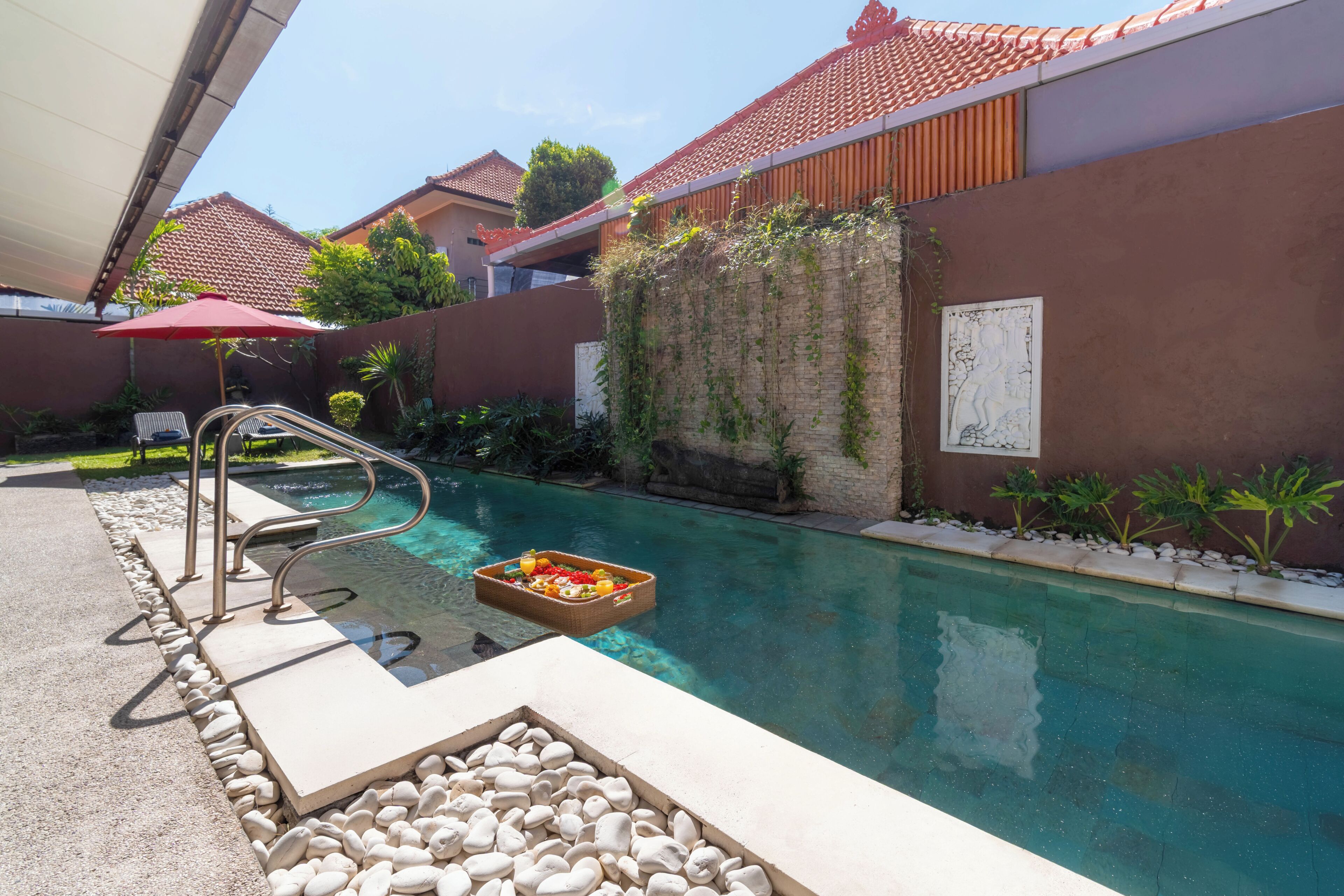 A swimming pool with a stone border, a metal ladder, and a basket of fruits.