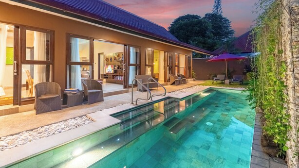 A swimming pool with a glass bottom, outdoor seating, and a building with large windows. - Nauli Villas Sanur (Denpasar)