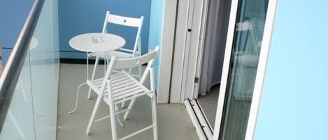 A balcony with a white table and chairs, a glass railing, and a sliding door.