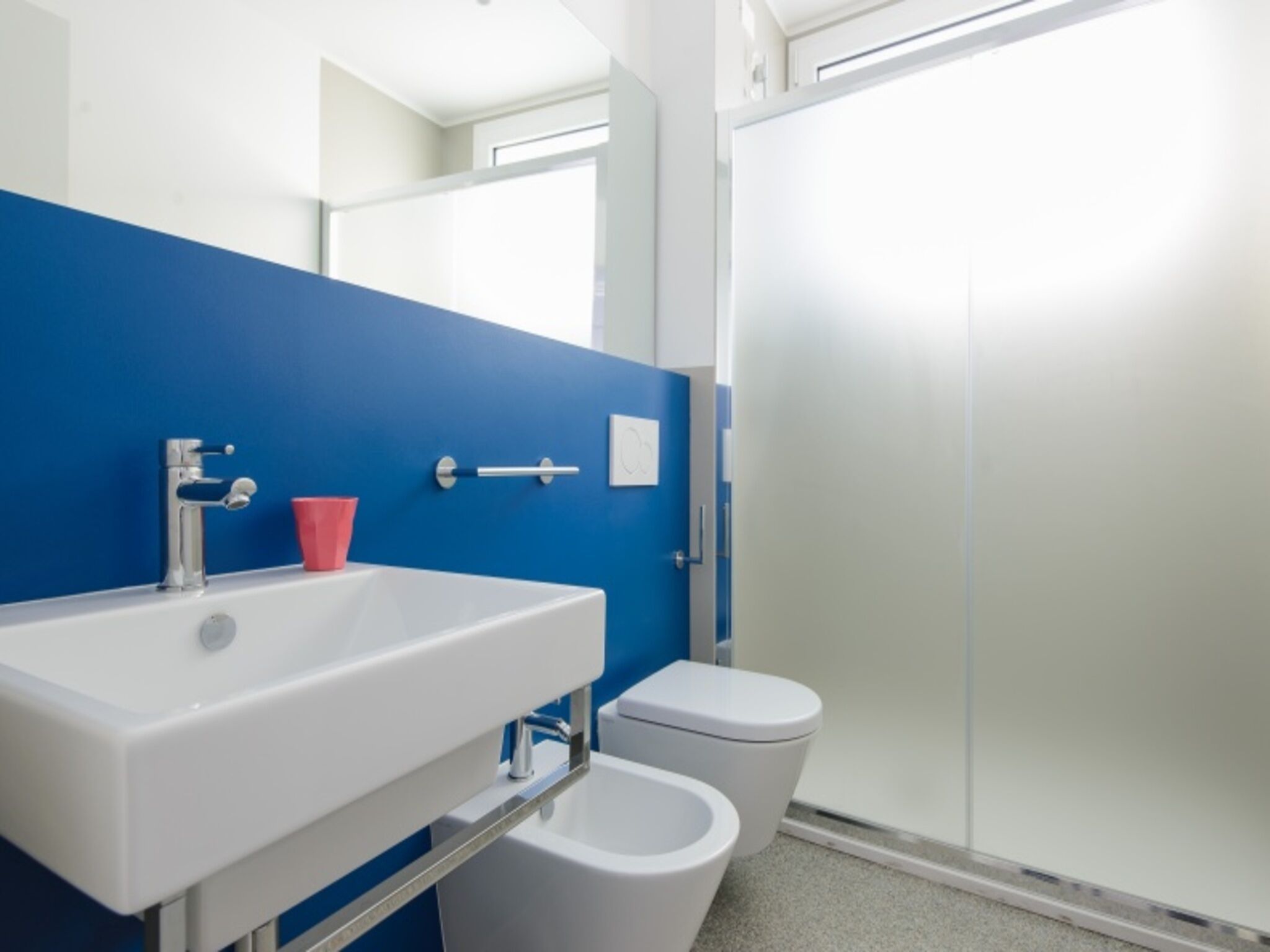Un baño con un lavamanos blanco, un inodoro y una pared azul.