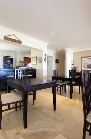 A dining area with a dark wooden table and chairs, a kitchen area with a counter and appliances, and a hallway with framed pictures. - Long-standing luxury guesthouse overlooking the Atlantic Ocean and Lion's Head. (Cape Town)