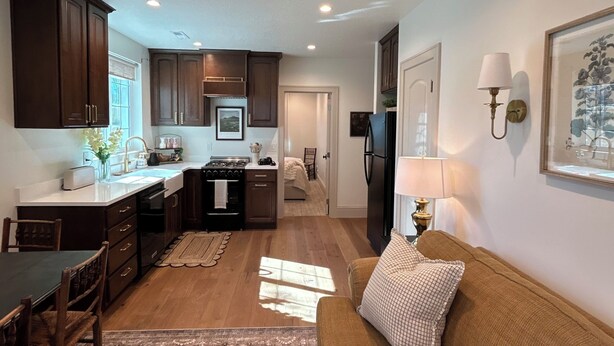 A modern kitchen with dark wooden cabinets, a dining area with a patterned rug, and a living room with a brown sofa.