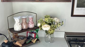 Une cuisine avec des meubles en bois, une cuisinière à gaz, une bouilloire, une étagère avec des bocaux et un vase rempli de fleurs.