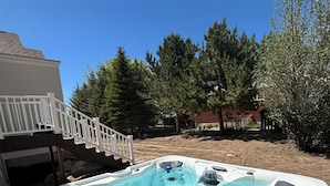 A hot tub with multiple jets, a white deck, and a staircase leading to a house.