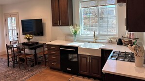 A kitchen with dark wooden cabinets, a white countertop, a built-in dishwasher, a window with a view, and a dining area with chairs and a table.